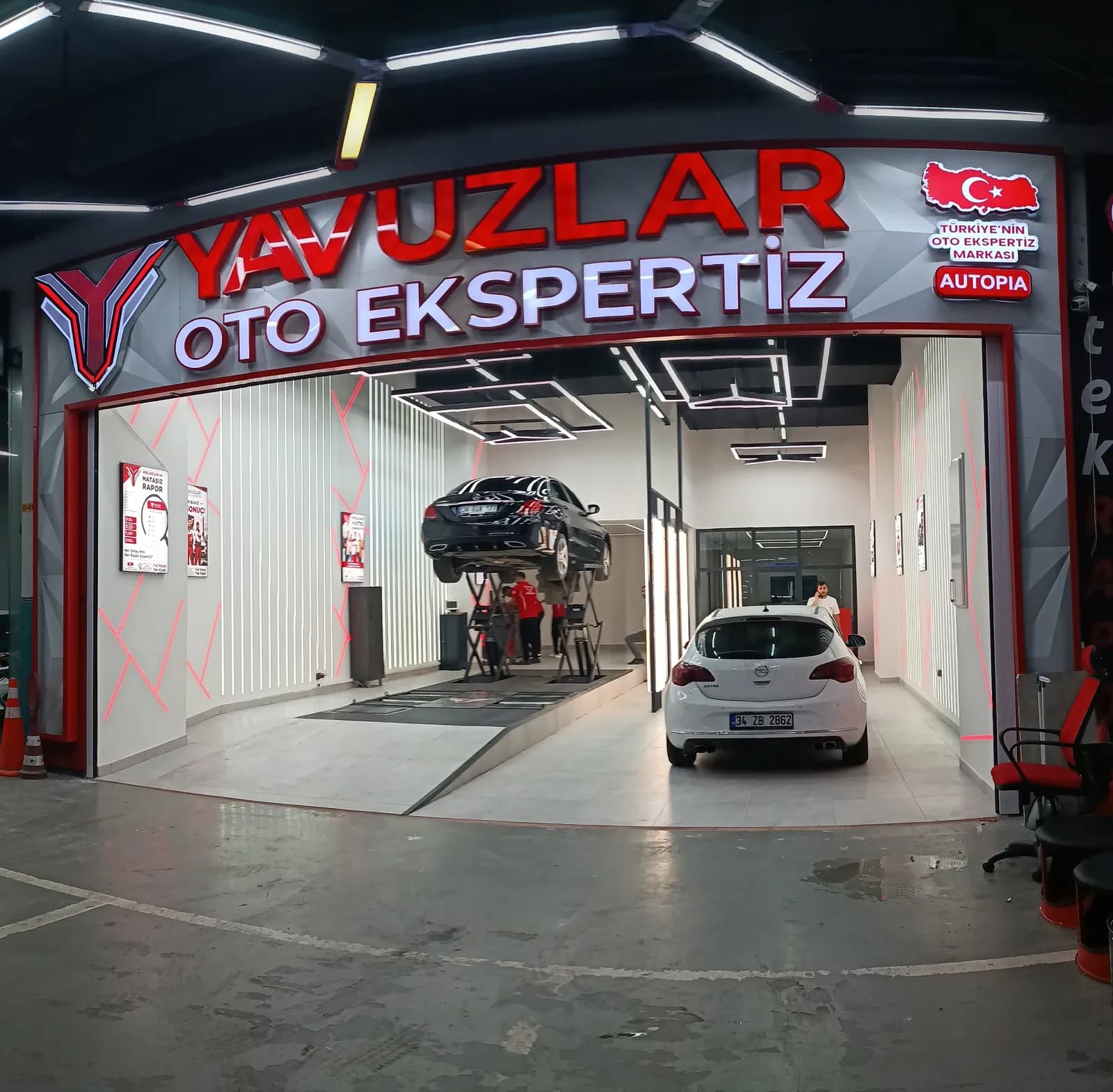Yavuzlar Autopia Oto Ekspertiz girişinin geniş açı görünümü — tabela, ekspertiz hattı ve liftteki araç